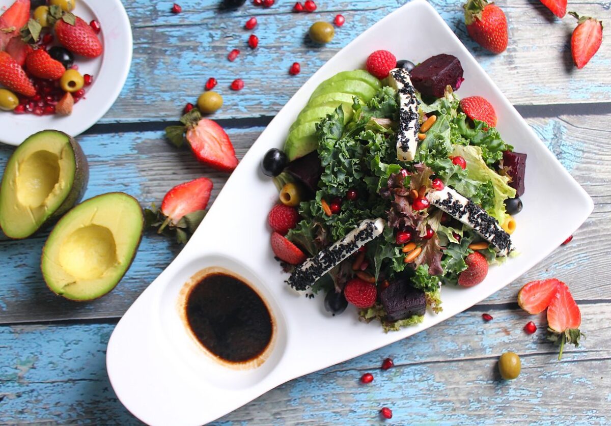 Fresh and nutritious salad featuring avocado, strawberries, and diverse greens, served on a white plate with rustic blue wooden background.
